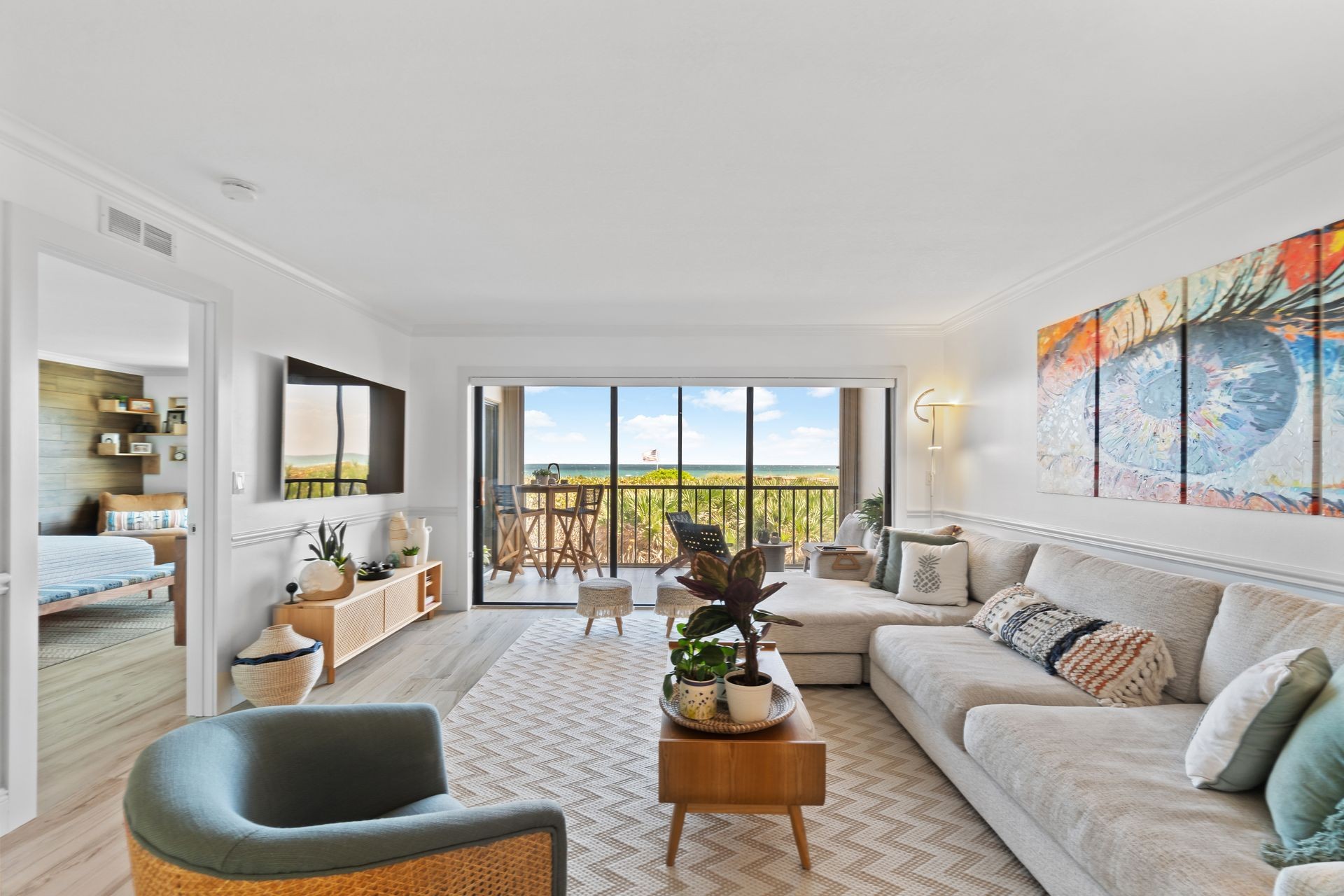 Modern living room with large sofa, artwork on the wall, and a balcony view of greenery.